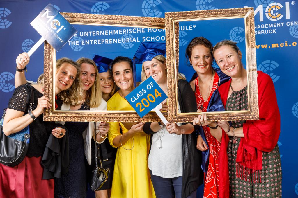 MCI Absolventinnen posieren mit einem Bilderrahmen vor blauen Hintergrund 