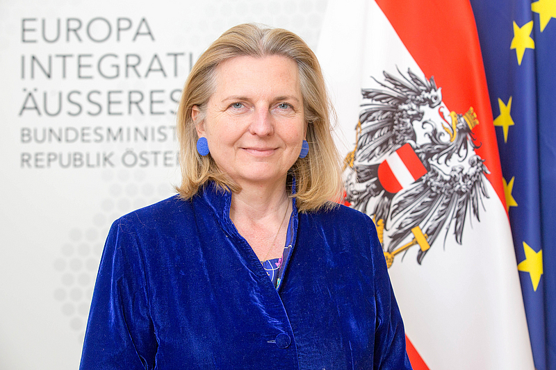 Karin Kneissl mit der österreichischen und europäischen Flagge im Hintergrund