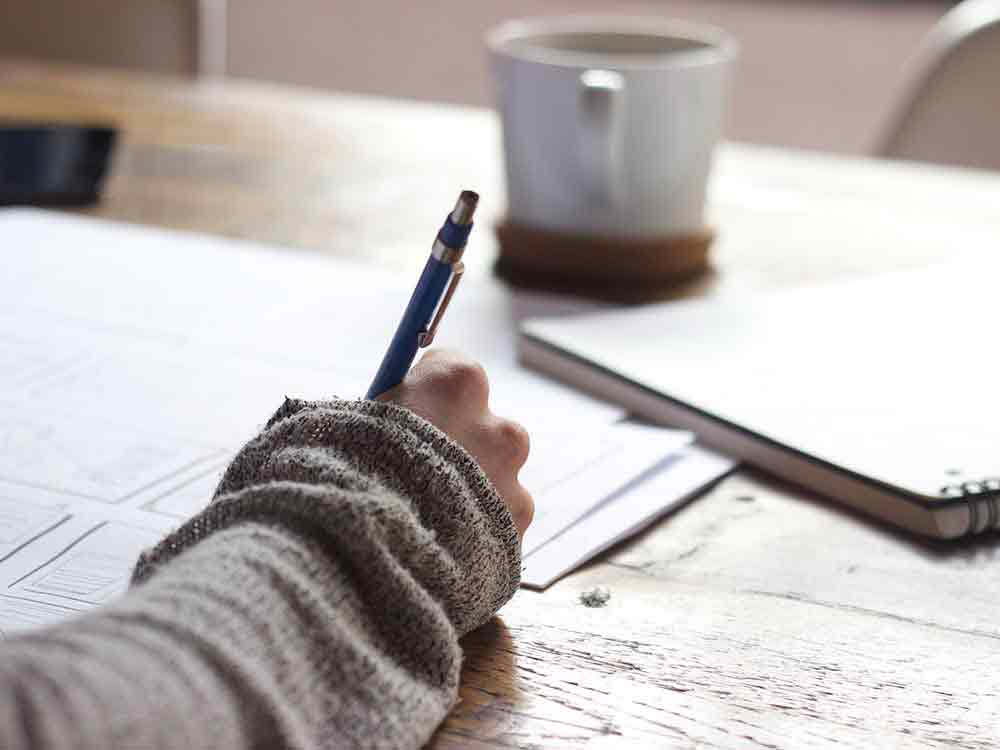 A person sits at a table and writes on a sheet of paper.